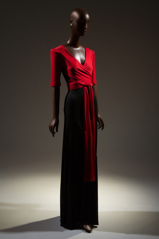Two-tone evening dress in red and black rayon jersey; red top with deep V-neck, short sleeves padded at cap, attached vest panel with wrap and tie extensions; long flared black skirt.