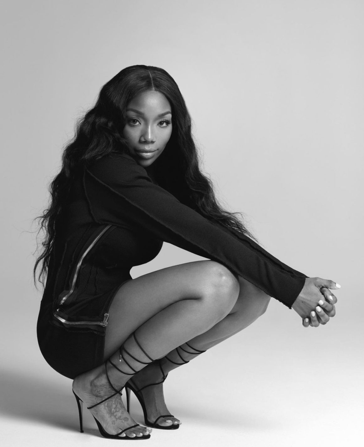 Brandy Stuns in Black and White Photoshoot Wearing Lionne Clothing Black Long Sleeve Zip Up Mini Dress and Femme LA Black Lace Up Sandals6