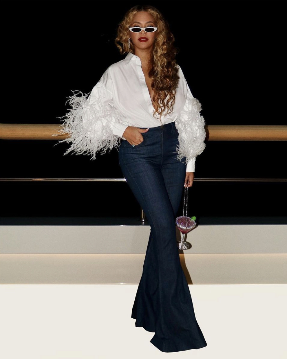 Beyonce Spotted Yachting in Capri With Jay Z Wearing Valentino White Feather Shirt Flare Leg Jeans PHILO White Sunglasses and Judith Leiber Martini Clutch