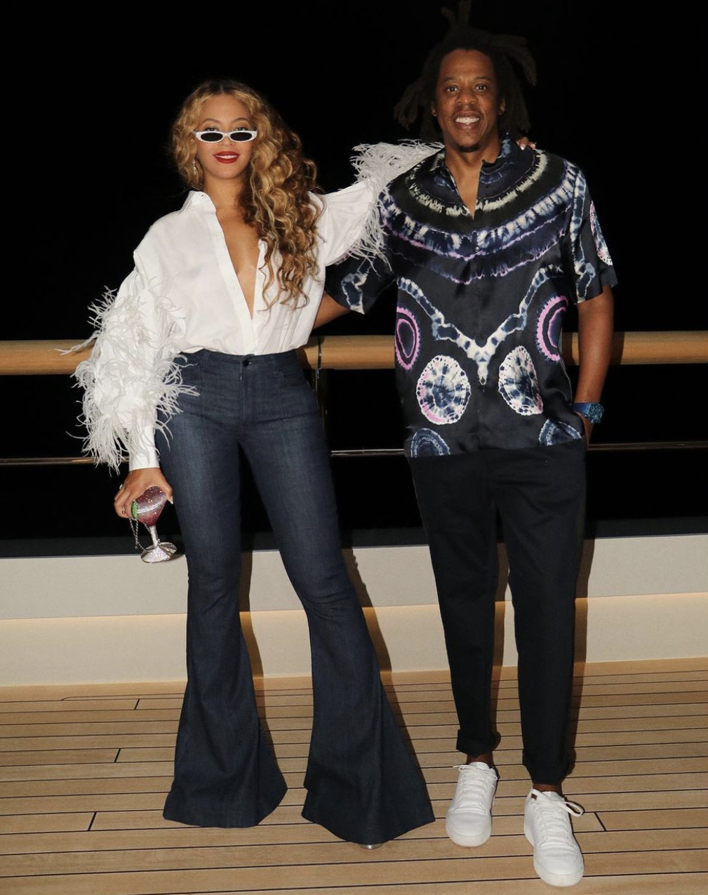 Beyonce Spotted Yachting in Capri With Jay Z Wearing Valentino White Feather Shirt Flare Leg Jeans PHILO White Sunglasses and Judith Leiber Martini Clutch4